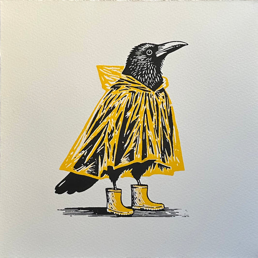 A black crow wearing a yellow raincoat and matching wellington boots. The contrast between the yellow outfit and the bold black crow creates a unique and whimsical image. This handmade linocut print makes a perfect gift for crow and bird lovers.