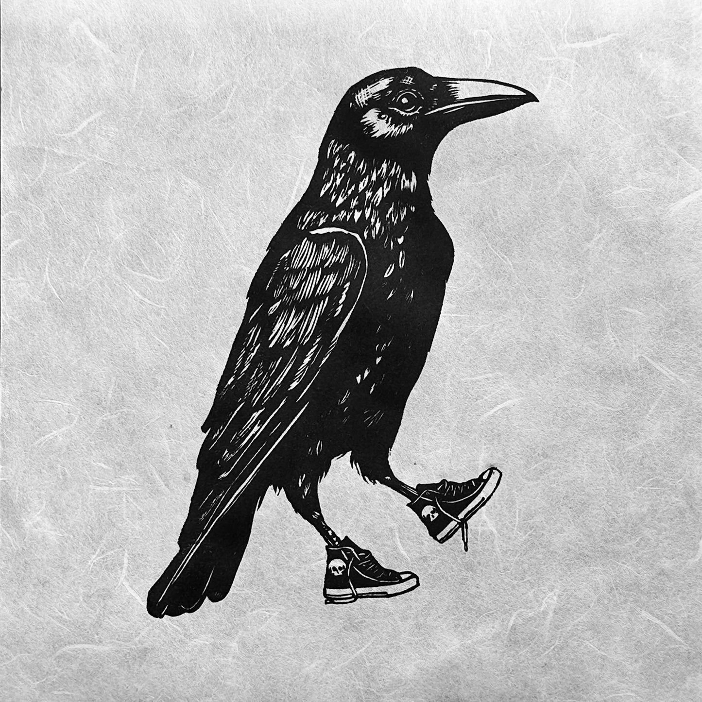 Handmade linocut print of a crow standing upright, wearing sneakers. The crow is detailed with bold, black ink lines, and its kicks/sneakers/trainers add a playful, whimsical touch to the artwork.